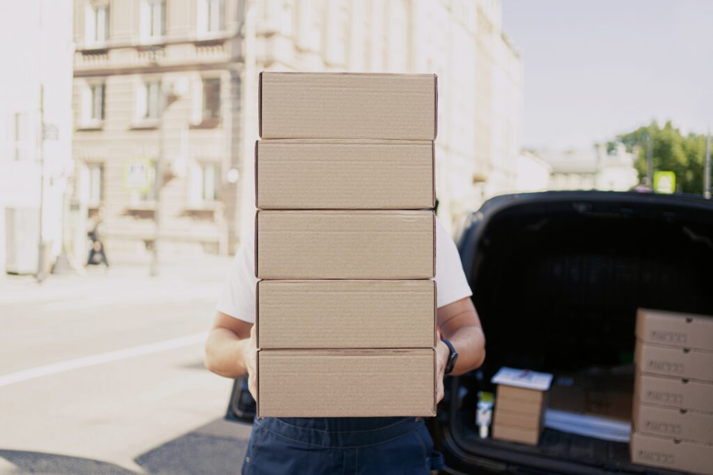 A courier worker picks up packing boxes that are being placed in the car.