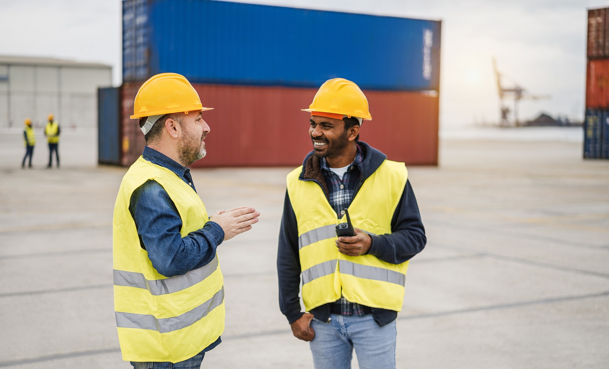 Multiracial workers controlling shipping containers at industrial port outdoor